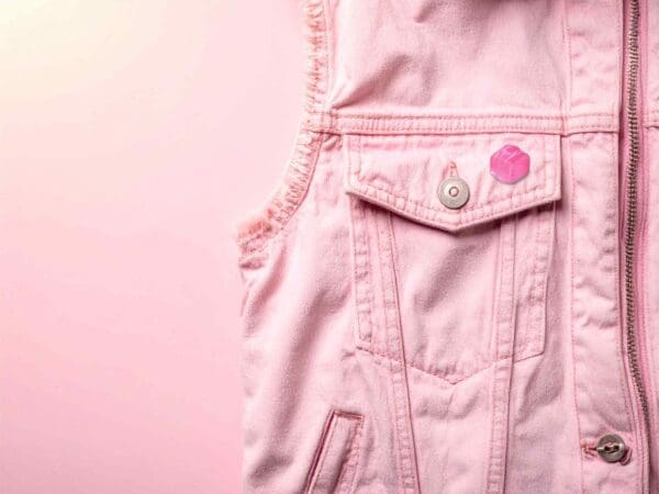 Pink French Fancy pin badge pinned pink denim gilet against a pink gradient background.