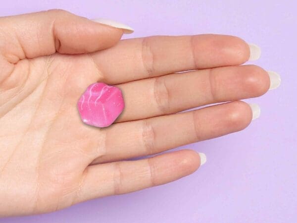 Pink French Fancy pin badge held in a woman's hand against a lilac gradient background.