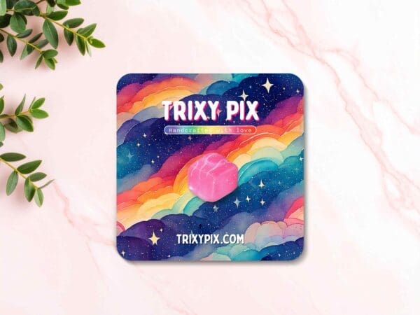 Pink French Fancy pin badge displayed on a marble pink background, attached to a backing card featuring rainbow-coloured clouds.
