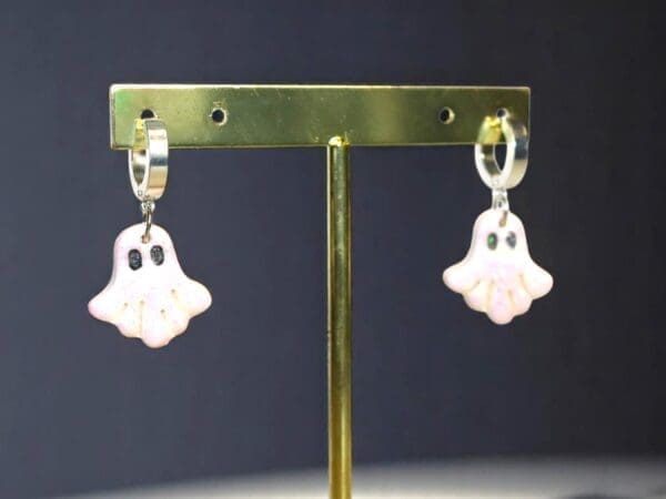 Polymer Clay Ghost earrings on a metal stand against a dark black background.