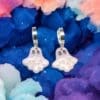 A pair of polymer clay ghost earrings against a rainbow coloured cloudy background.