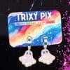 Polymer clay ghost earrings attached to a colourful backing card against a black background surrounded by pink glitter.