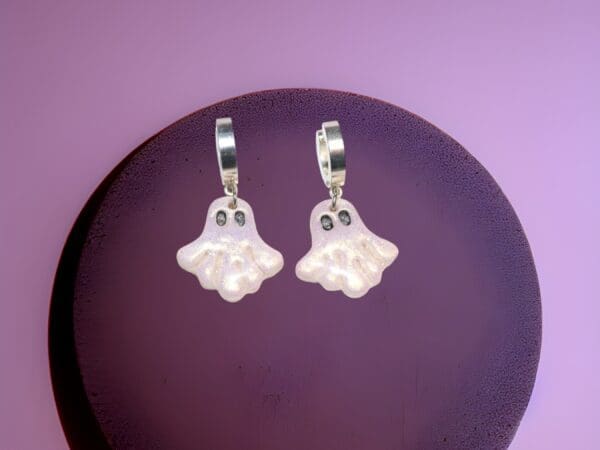 A pair of polymer clay ghost earrings against a dark purple background.
