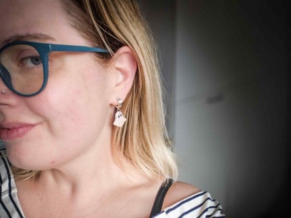 A woman wearing a polymer clay ghost earring. The lady's head is turned to the side.